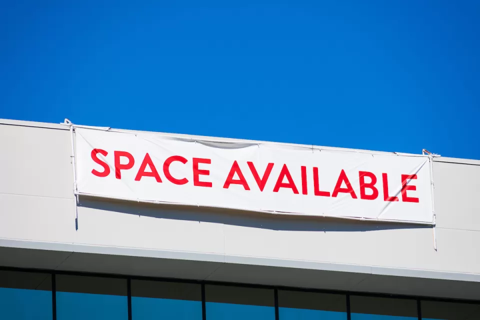 White banner with red "SPACE AVAILABLE" text hanging at top of white office building.